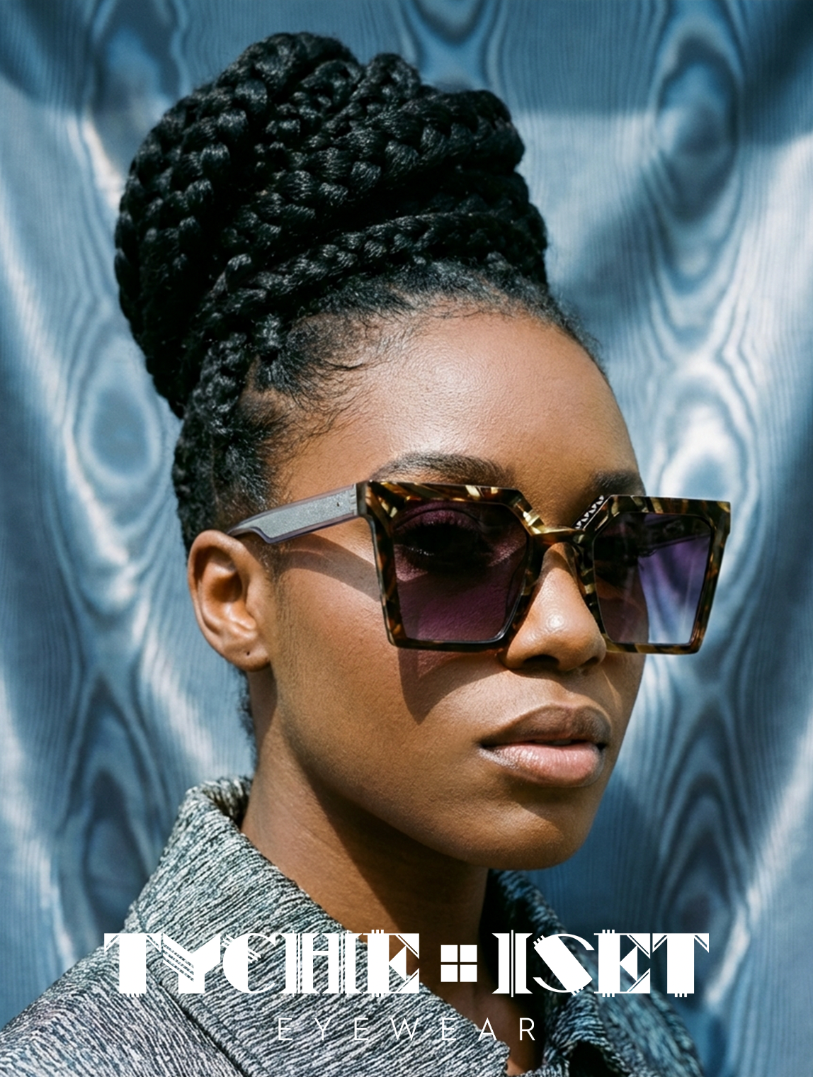 Woman wearing square framed sunglasses with a textured blue background, featuring the brand 'Tyche & Iset'.