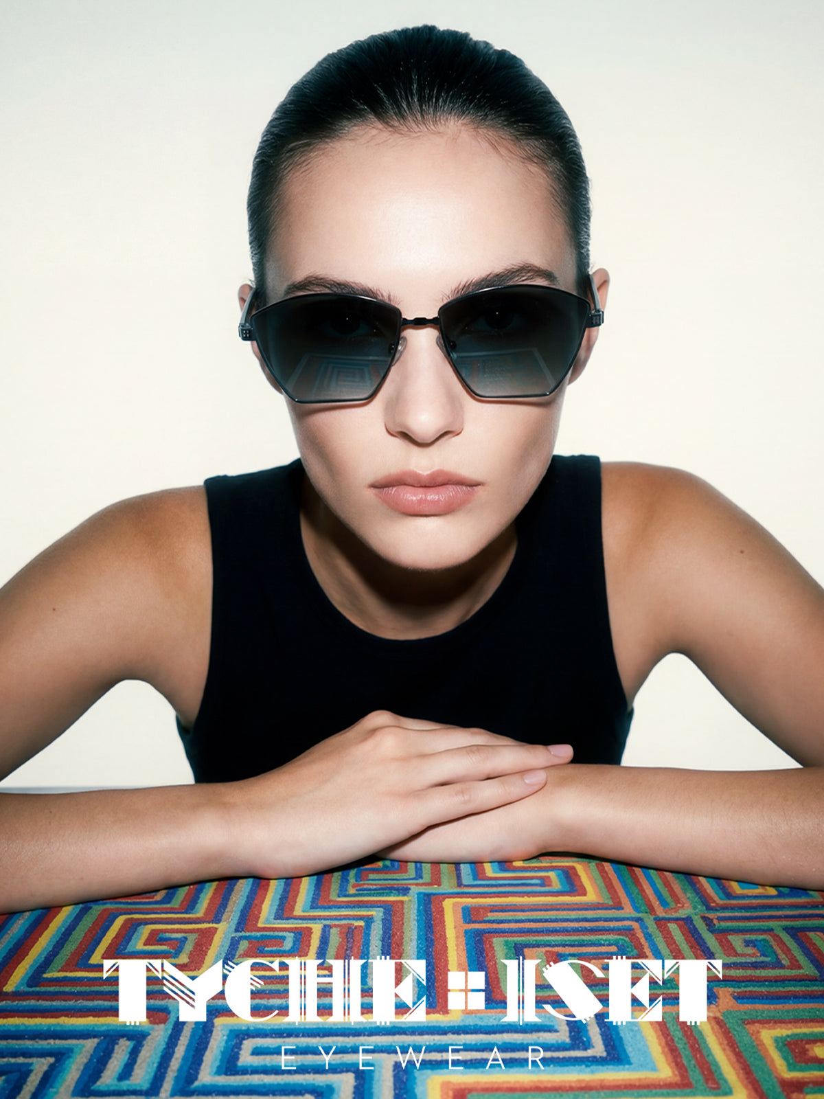 portrait of woman wearing sunglasses with a colorful geometric patterned surface and 'Tyche & Iset' logo, luxury eyewear